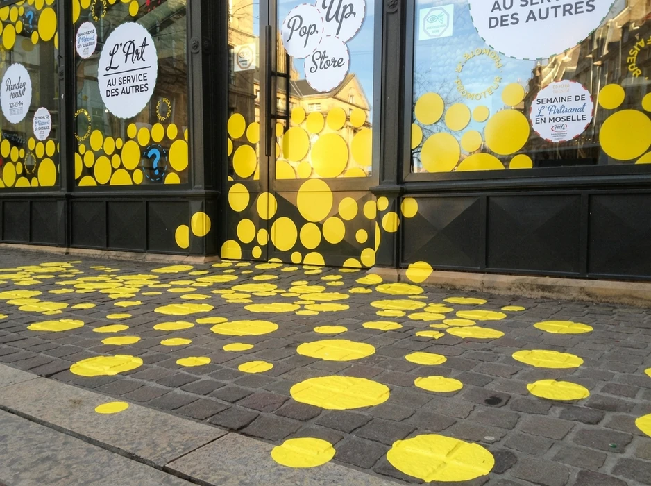 Devanture de commerce en extérieur décorée de disques adhésifs jaunes vifs, collés sur les vitrines, la porte et le sol en pavés