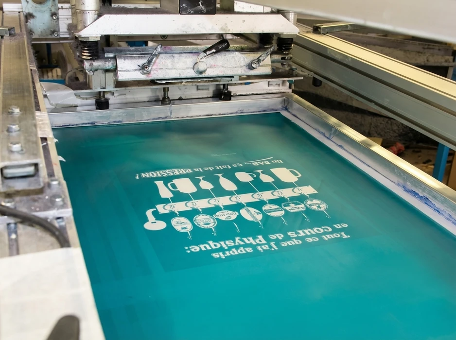 Atelier de sérigraphie industrielle, vue rapprochée d'un cadre sérigraphique tendu d'un écran mesh turquoise sur une table d'impression automatique