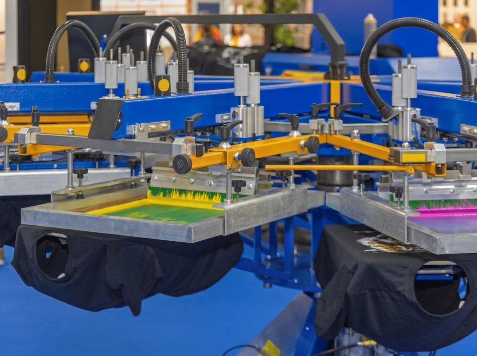 Machine à broder industrielle multi-aiguilles en action, brodant un logo sur tissu noir tendu dans un tambour circulaire turquoise